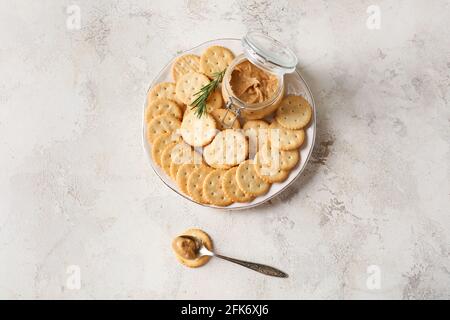 Piatto con gustosi cracker e vaso con burro di arachidi su sfondo chiaro Foto Stock
