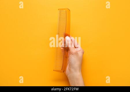 Mano femminile con pettine in plastica su sfondo colorato Foto Stock