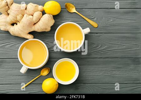 Tazze di tè con zenzero, miele e limoni su sfondo di legno scuro Foto Stock