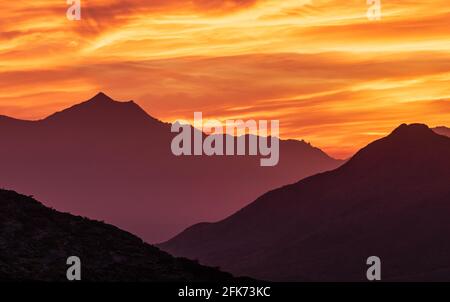 Il Fiery cielo sopra le montagne desertiche frastagliate Foto Stock