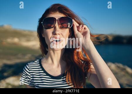 donna allegra che indossa occhiali da sole montagne all'aperto vicino al mare Foto Stock