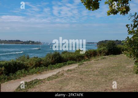 Vista sull'oceano che si apre tra due isole. Le barche a vela vanno al mare. In primo piano si trova una strada sterrata che gira a destra. Foto Stock