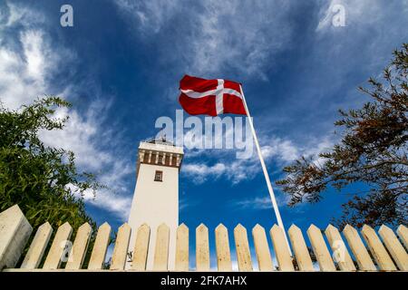 La bandiera danese vola di fronte al faro di Helnaes. Helnæs, Danimarca Foto Stock