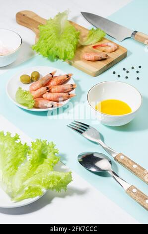 Insalata di verdure fresche, gamberi con ombra in luce dura su color menta pastello e tavolo di legno bianco. Cibo sano estivo in stile moderno di colore. Foto Stock