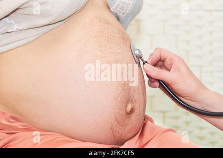 il medico esamina una donna incinta ascoltando il feto battito cardiaco con fonendoscopio Foto Stock