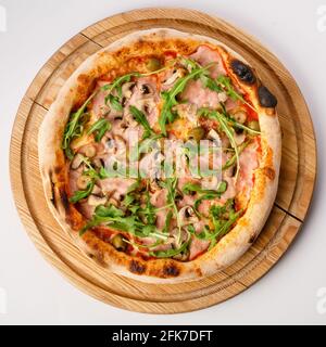 Vista dall'alto della pizza calda su un piedistallo in legno. Pizza Capricciosa , base di pomodoro. Tenere il prosciutto, i funghi, le olive e l'rucola fresca a base di due chee Foto Stock