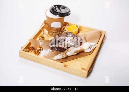 I biscotti al cioccolato giacciono su carta kraft e caffè su un vassoio rustico di legno su sfondo bianco. Tazza di carta e stoviglie monouso in materiale ecologico Foto Stock
