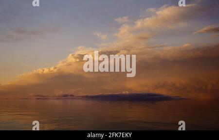 Il cielo del tramonto con le nuvole e la luce solare si riflettono sulla superficie dell'acqua. Foto Stock