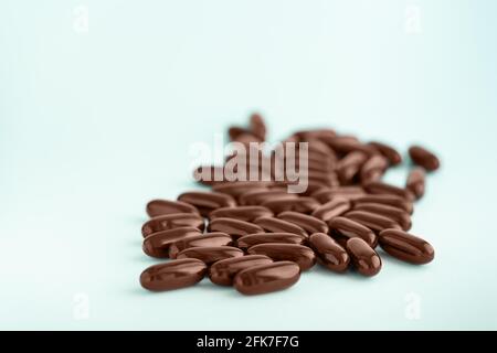Capsule marroni, pillole di gel con olio isolato su sfondo blu. Integratori nutrizionali per perdita di peso ed energia, aiuti alimentari. Foto Stock