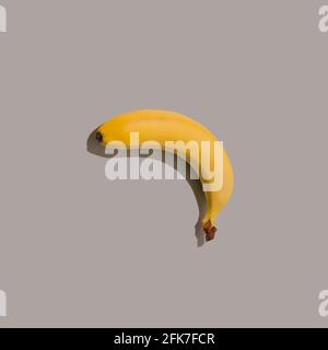 Banana gialla su sfondo grigio. Concetto di cibo minimale e divertente. Unica idea astratta di posa piatta. Foto Stock