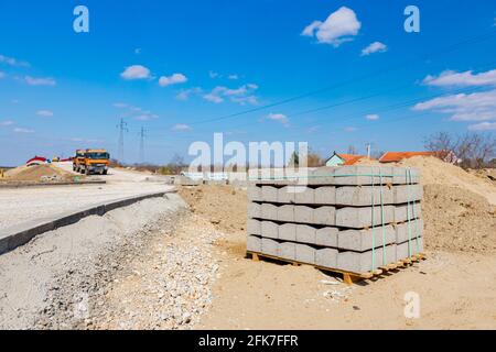 Pila di pietre di confine imballate per asfalto su pallet di legno in cantiere. Foto Stock