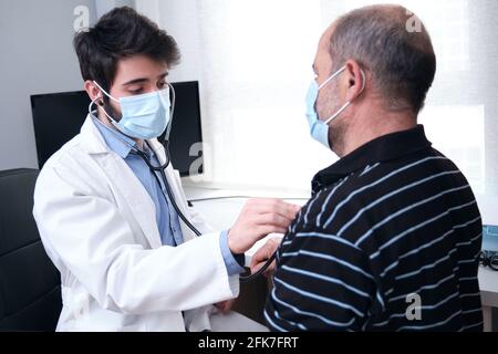 Giovane medico sanitario fornitore di eseguire un esame fisico e ascoltare l'uomo maturo paziente cuore e polmoni con uno stetoscopio. Foto Stock