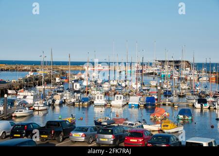 Yorkshire, UK – 10 ago 2017 : una fila di auto si affaccia su un porto trafficato pieno di barche a vela colorate, la flotta di Bridlington Harbour Foto Stock