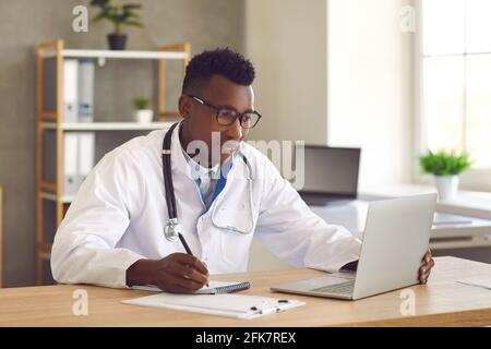 Medico medico professionista che guarda lo schermo del portatile e scrivere note su carta Foto Stock