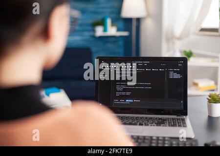 Giovane programmatore che scrive codice di programma virtuale per lo sviluppo di software e applicazione mobile su computer portatile, studente programmazione JavaScript mentre si siede al tavolo da tavolo in soggiorno Foto Stock