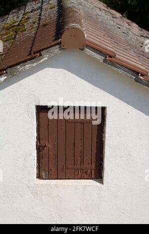Chiuso tetto finestra di legno marrone su una facciata bianca di una piccola casa Foto Stock