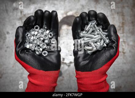 La persona che indossa guanti protettivi che tengono una manciata di bulloni e. dadi su fondo metallico Foto Stock