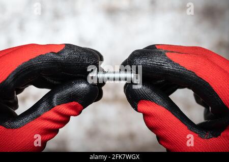 Persone che indossano guanti di protezione che trattengono il bullone e il dado contro il metallo sfondo Foto Stock