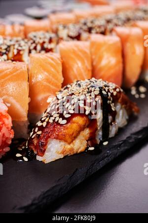 Un pezzo di sushi nigiri si trova su una tavola di pietra nera su uno sfondo di Rolls Philadelphia. Concetto di deliziosa cucina tradizionale giapponese, delici Foto Stock