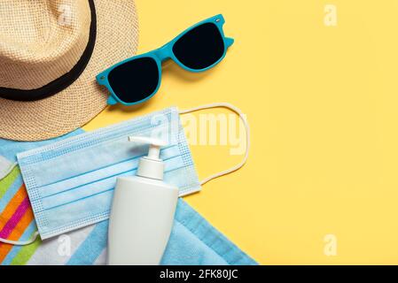 Maschera chirurgica protettiva con occhiali da sole, cappello e bottiglia di plastica di protezione solare Con copy space su sfondo giallo.Summer Concept con covid-19 Foto Stock