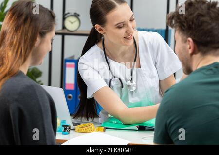 Un ginecologo sta spiegando i risultati dei test a una paziente incinta. Una coppia sposata nell'ufficio del ginecologo. Foto Stock