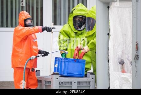 29 aprile 2021, bassa Sassonia, Hildesheim: I vigili del fuoco in tute di protezione si trovano all'esterno di una grande lavanderia durante un'operazione. Un tamburo gonfiato da 200 litri di sostanze chimiche in una lavanderia a Hildesheim ha innescato un'operazione di vigili del fuoco. La sostanza chimica era ipoclorito di sodio - un agente sbiancante e disinfettante. Foto: Julian Stratenschulte/dpa Foto Stock