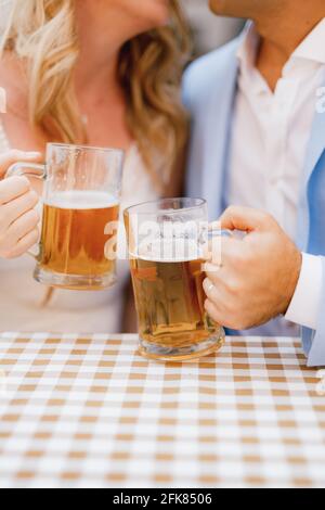 Un uomo e una donna sono seduti abbracciandosi l'un l'altro al tavolo e tenendo tazze di birra in loro mani Foto Stock