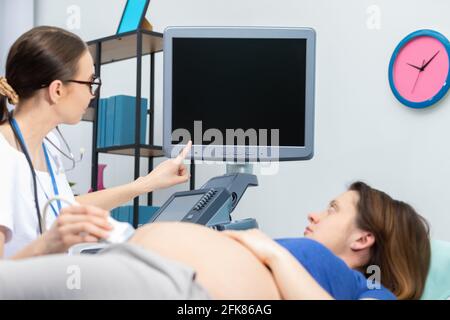 Un medico di signora mostra ad un paziente incinta il suo bambino non ancora nato sullo schermo a ultrasuoni. Ufficio di Ginecologia. Foto Stock