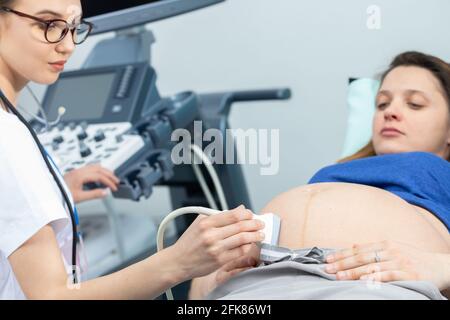 Nella sala di ginecologia, un medico di signora esamina una donna incinta utilizzando una macchina ad ultrasuoni. Foto Stock