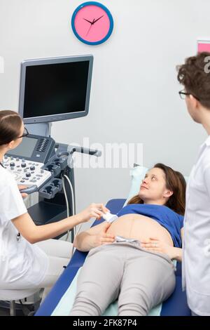 Un infermiere esegue un'ecografia su una paziente incinta sotto la guida del medico curante. Foto Stock
