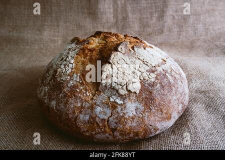 primo piano di pane fresco rotondo di pane integrale sano su fondo di tessuto di juta marrone con farina bianca sulla parte superiore. vista superiore del pane fatto in casa o Foto Stock