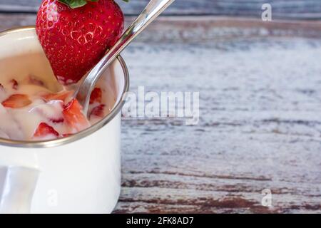 Delizioso spuntino estivo con yogurt alla fragola appena fatto servito una tazza di smalto bianco su sfondo di legno con spazio di copia Foto Stock