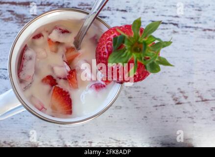 Vista panoramica su un delizioso yogurt fatto in casa con fragole fresche in una tazza di smalto bianco su sfondo di legno bianco tesse con spazio per la copia Foto Stock