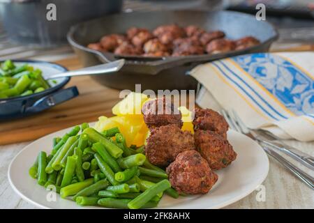 pasto fresco cotto in casa con polpette fritte, fagioli verdi e patate bollite serviti su un piatto con padella sullo sfondo sul tavolo da cucina Foto Stock