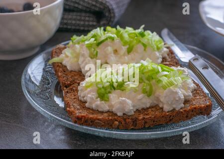 Ancora vita di un fresco preparato panino aperto con formaggio di cottage e erba cipollina su un piatto di vetro servito un tavolo da cucina per la colazione Foto Stock
