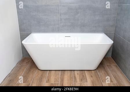 Una moderna vasca indipendente a parete, senza rubinetto, in un bagno rivestito di piastrelle in ceramica. Foto Stock