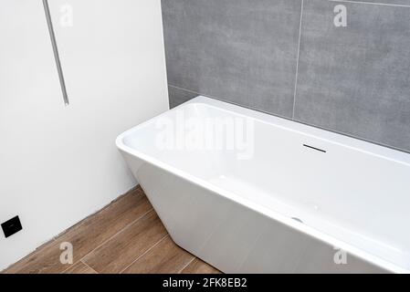 Una moderna vasca indipendente a parete, senza rubinetto, in un bagno rivestito di piastrelle in ceramica. Foto Stock