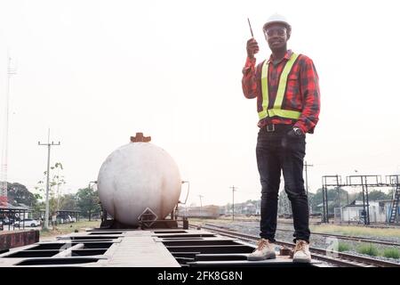 L'ingegnere africano maschile controlla un treno su ferrovia con conversazione tramite comunicazione radio o walkie talkie Foto Stock