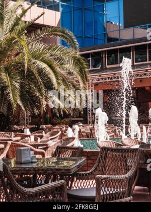 Tavoli vuoti nel caffè o nel ristorante all'aperto, con palme e fontana. Interno Street cafe. Concetto di vacanza e resort. Verticale. Foto Stock