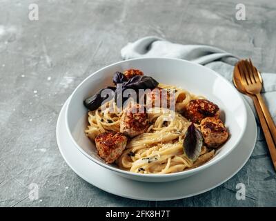 Polpette di parmigiano con pasta Carbonara in piatto bianco su fondo grigio. Primo piano vista della carbonara cremosa con spazio copia a sinistra Foto Stock