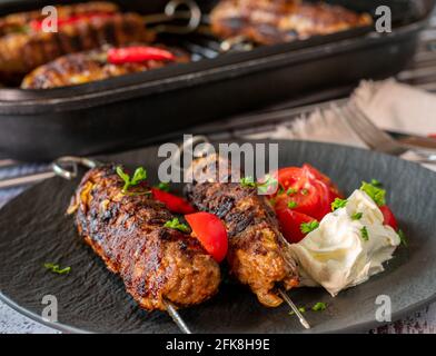 kebab di shish fresco fatto in casa su spiedini serviti con pomodori e panna acida su un piatto scuro sul tavolo da cucina sfondo Foto Stock