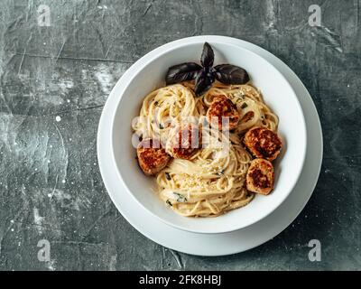 Polpette di parmigiano con pasta Carbonara in piatto bianco su fondo grigio. Primo piano vista della carbonara cremosa con spazio copia a sinistra. Vista dall'alto o piatta. Foto Stock