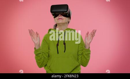 Donna anziana elegante e granny che usa l'app casco per le cuffie per giocare Simulazione di un gioco VR in realtà virtuale Foto Stock