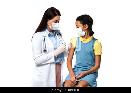 Pediatra in maschera medica facendo iniezione di vaccino ad afroamericano bambino isolato su bianco Foto Stock