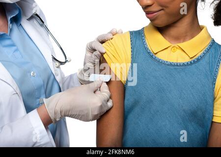 Vista ritagliata del medico che applica l'intonaco adesivo sul braccio di capretto afroamericano isolato su bianco Foto Stock
