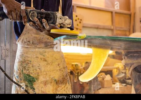 Primo piano di un artigiano africano tavola da surf Shaper lavorare in un'officina di riparazione Foto Stock