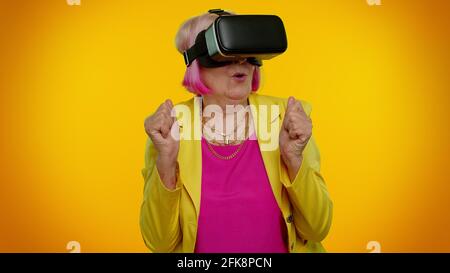 Donna anziana elegante e granny che usa l'app casco per le cuffie per giocare Simulazione di un gioco VR in realtà virtuale Foto Stock