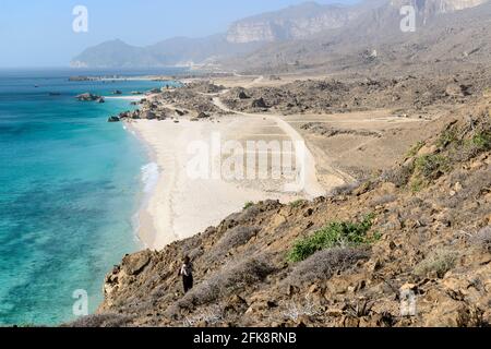 Turista occidentale che ammira la spiaggia di Fazaya dalle rocce sopra, Dhofar Governatorato, Oman Foto Stock