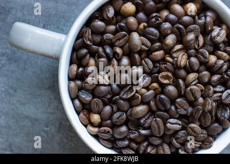 Primo piano di chicchi di caffè tostati interi in una tazza su sfondo grigio; bevanda calda; ingrediente Foto Stock