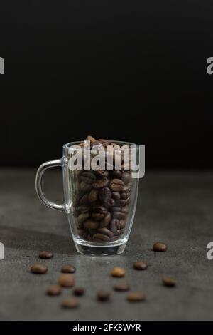 Primo piano di chicchi di caffè tostati interi in una tazza su sfondo grigio; bevanda calda; ingrediente Foto Stock